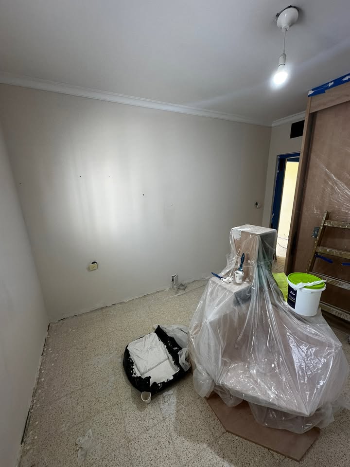 חדר עם קירות מוחלקים בגמר אחיד, כלי עבודה ודלי צבע מכוסים ביריעה